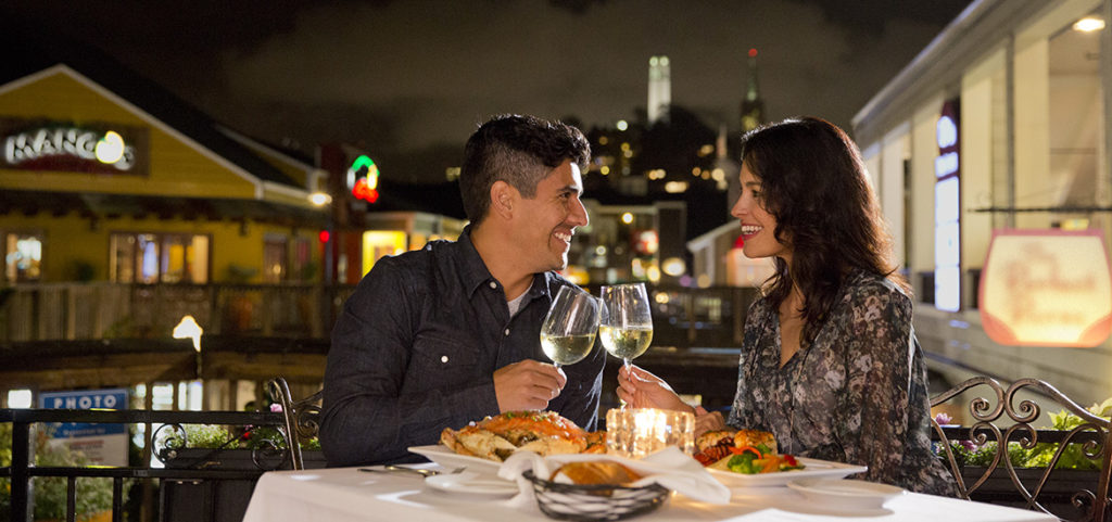 Couple enjoying dinner at night with wine and seafood and city in background