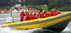 People in red jackets and lifevests about Bay Voyager yellow boat waving at camera