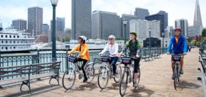 Four people riding tandem bike with San Francisco skyline in background