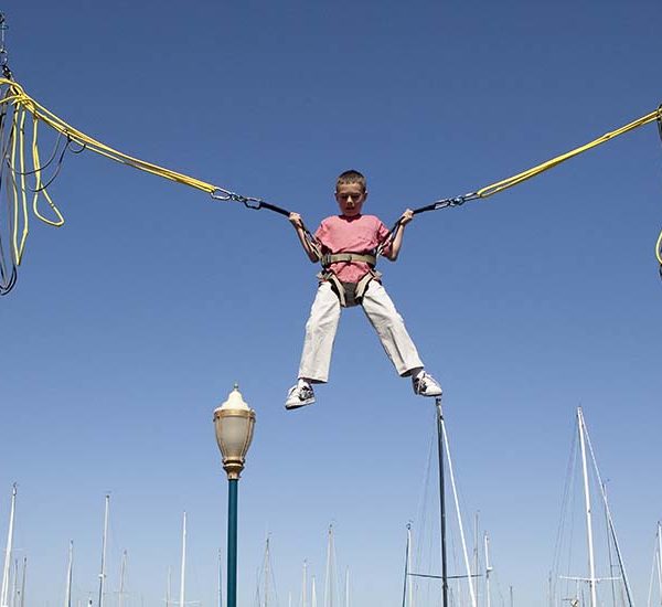 Boy in red shirt and white pants in air on bungee ride